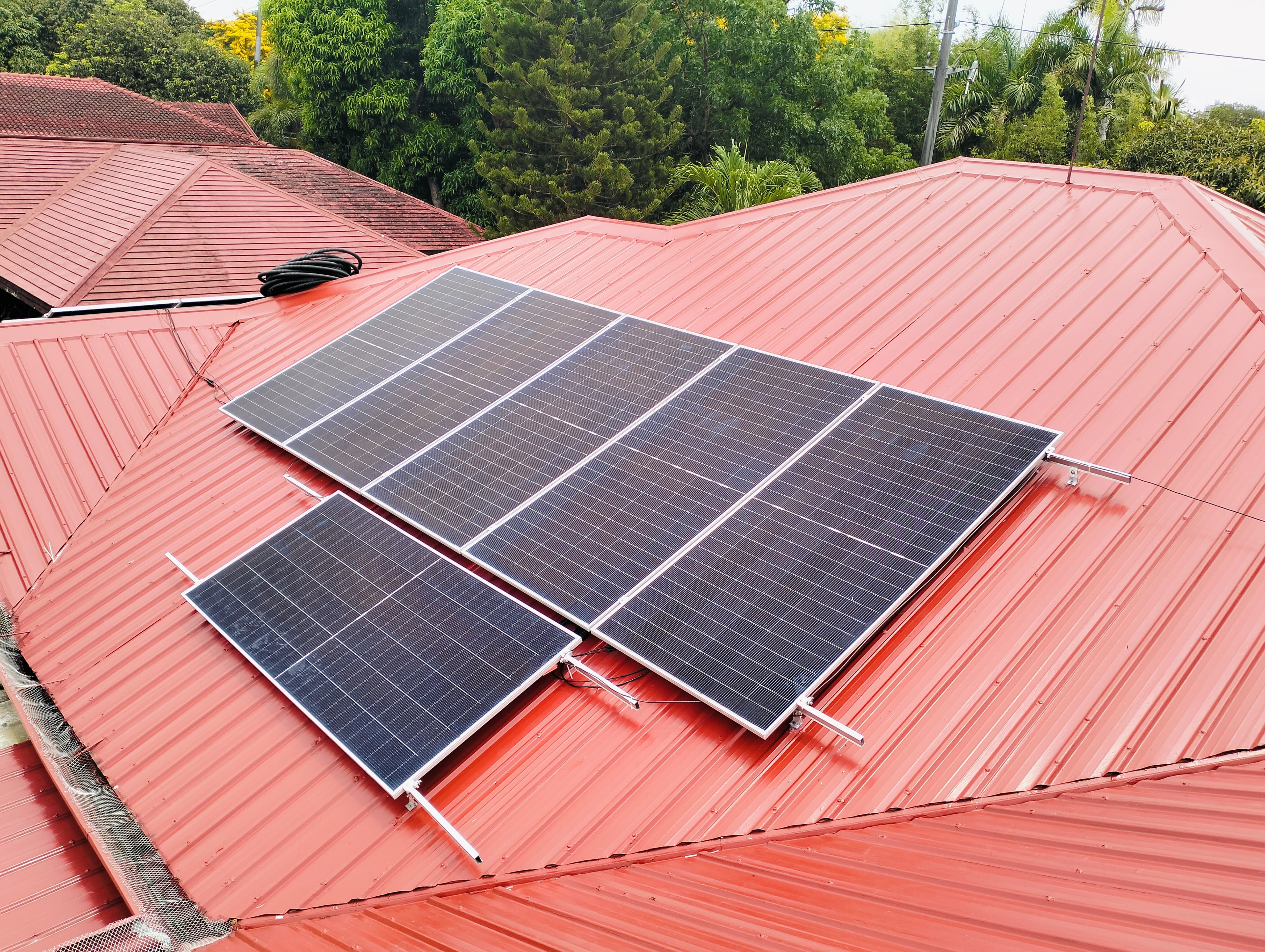 Solar panels mounted flush to the red metal roof of the Makati home, with the surrounding neighbourhood behind.